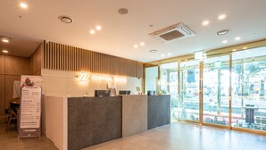 A hotel reception desk with a modern design, a clear view of the outside through large windows, and a sign indicating the hotel name. - Hotel ZINC (Seogwipo)