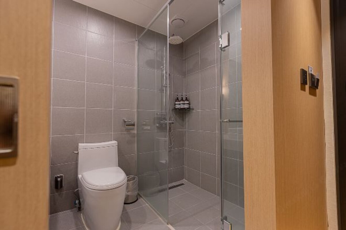 A modern bathroom with a toilet, a glass shower enclosure, and a wall-mounted towel dispenser.
