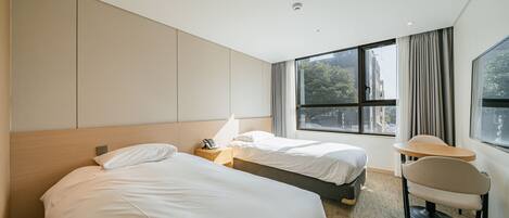 A hotel room with two beds, a small table, a chair, and a large window with curtains.