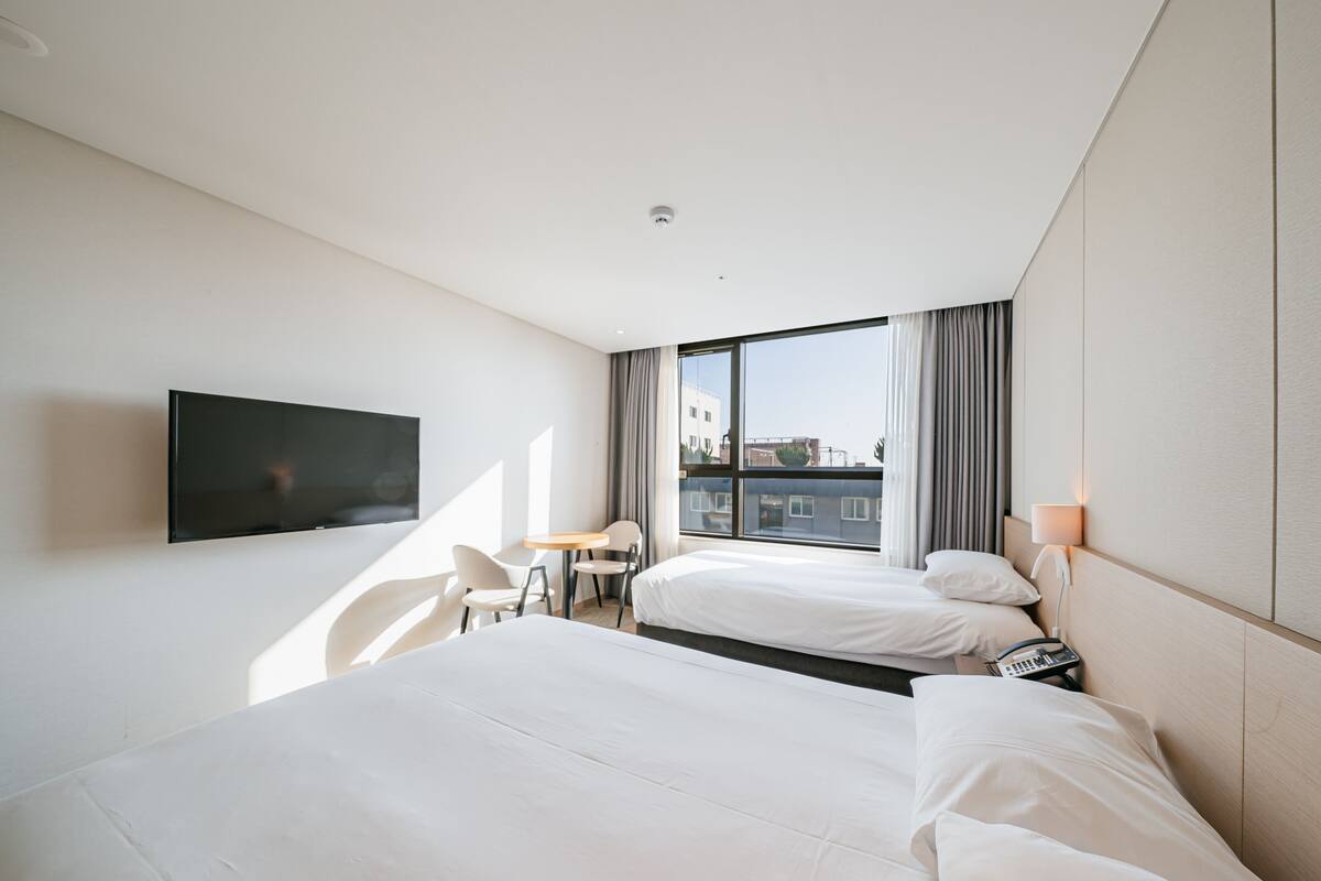 A hotel room with two beds, a TV mounted on the wall, a small table, and a chair.