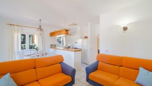A modern living room with two orange sofas, a kitchen area with a wooden countertop, and a dining area with white chairs. - 0306 Villa Monte Verde Granada (Javea / Xàbia)