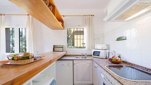 A compact kitchen with white appliances, a wooden countertop, and a window with bars. - 0306 Villa Monte Verde Granada (Javea / Xàbia)