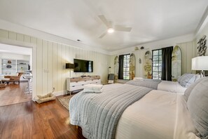 Een slaapkamer met een groot bed, een televisie, een plafondventilator en een raam met gordijnen.