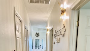 Passadís amb sòl de fusta, parets blanques i una porta amb interruptor de llum a la paret.