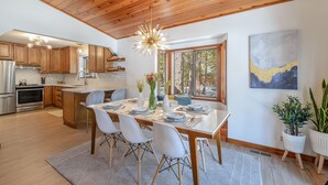 Une cuisine moderne avec des meubles en bois, un îlot central et un coin repas avec une table dressée pour quatre personnes.