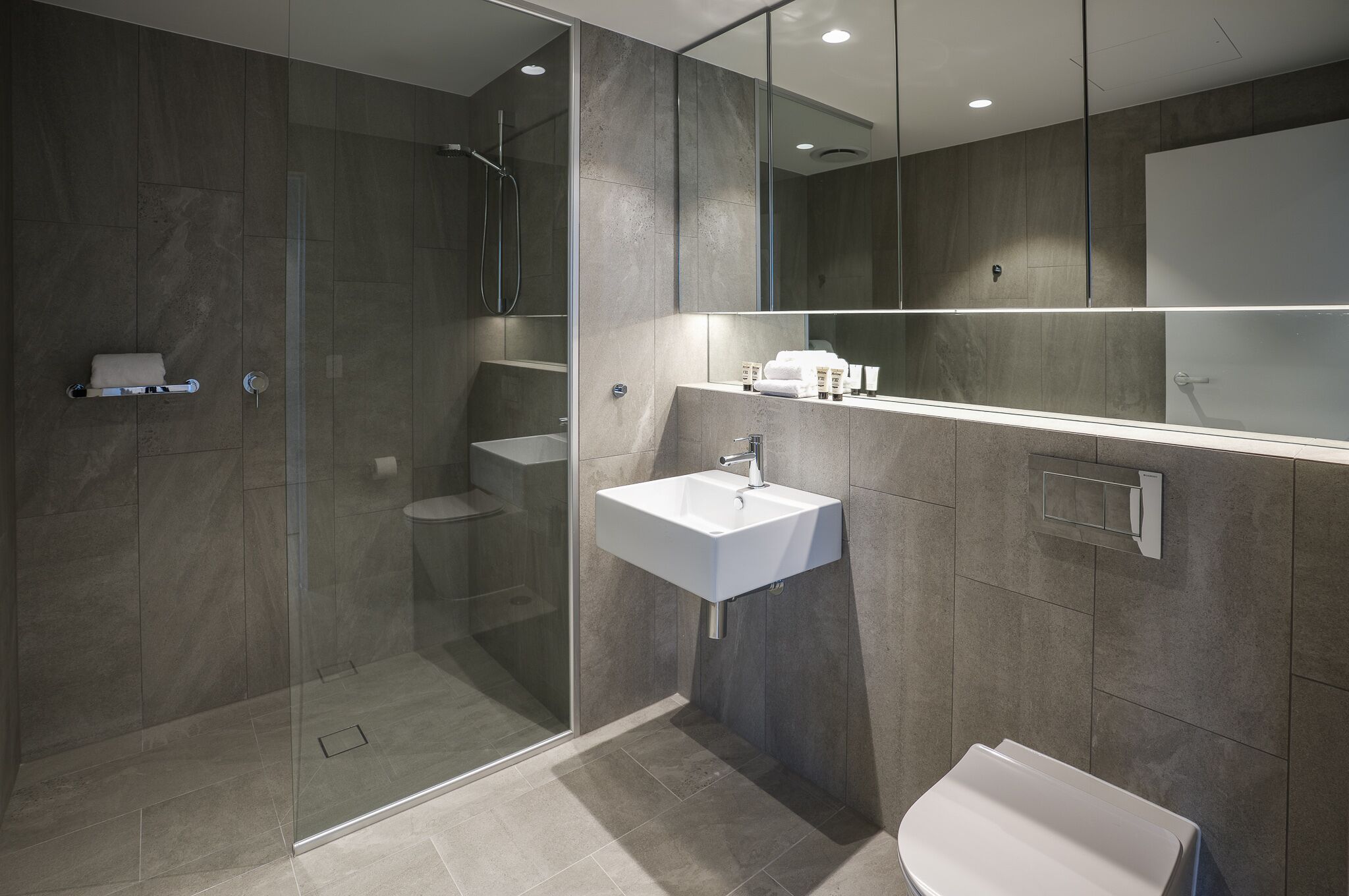 A modern bathroom with a glass-enclosed shower, a white sink, and a large mirror.