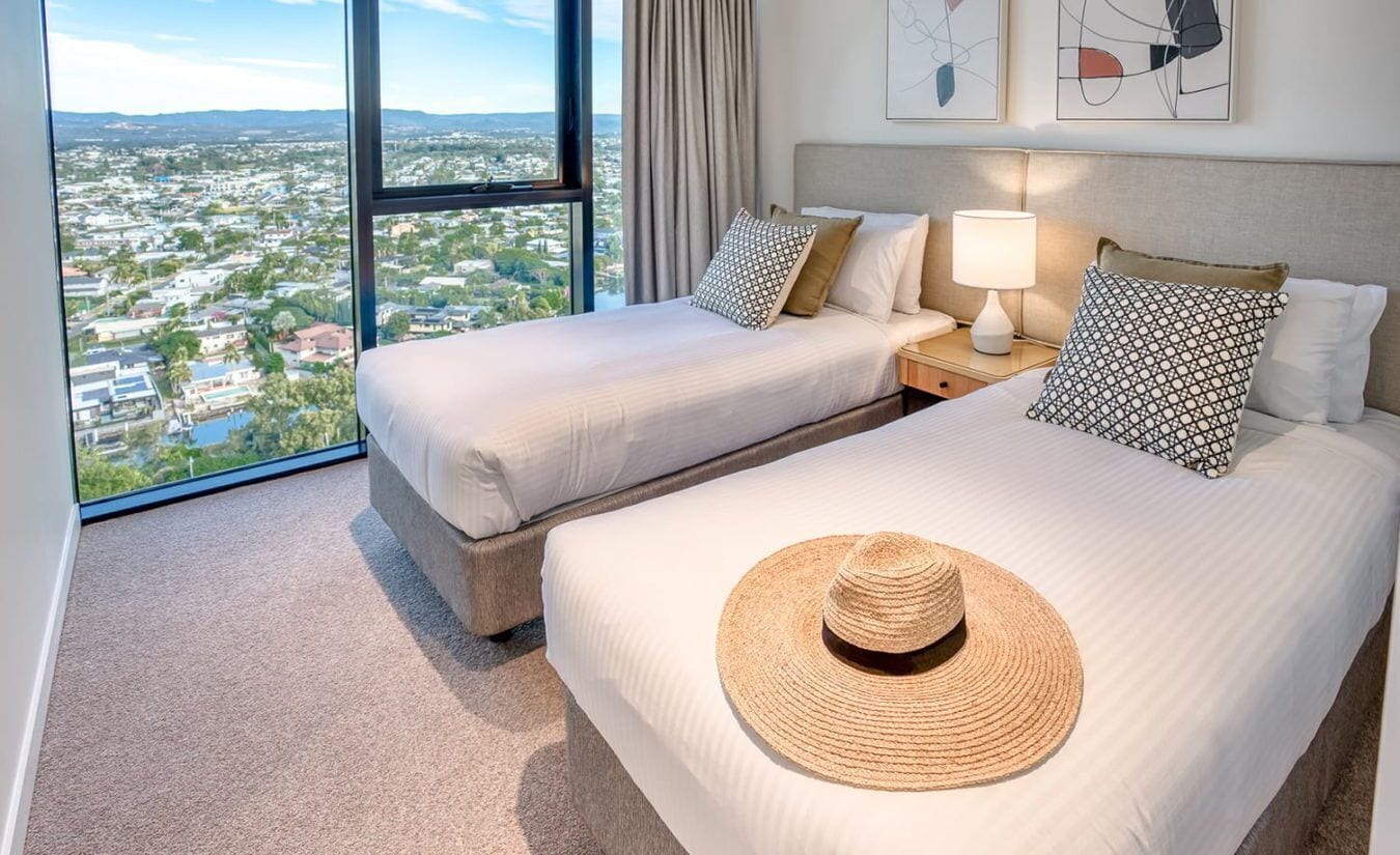 A hotel room with two beds, a view of a cityscape, and a large window.