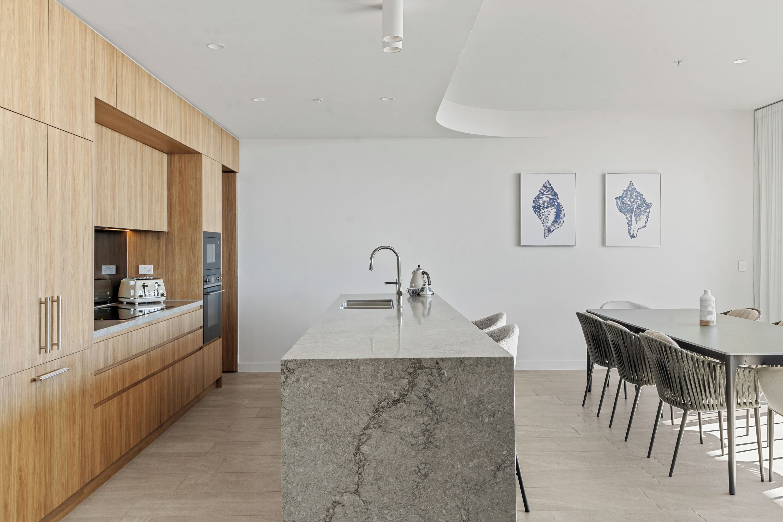 Una cocina moderna con armarios de madera, una isla de mármol y un comedor con sillas.