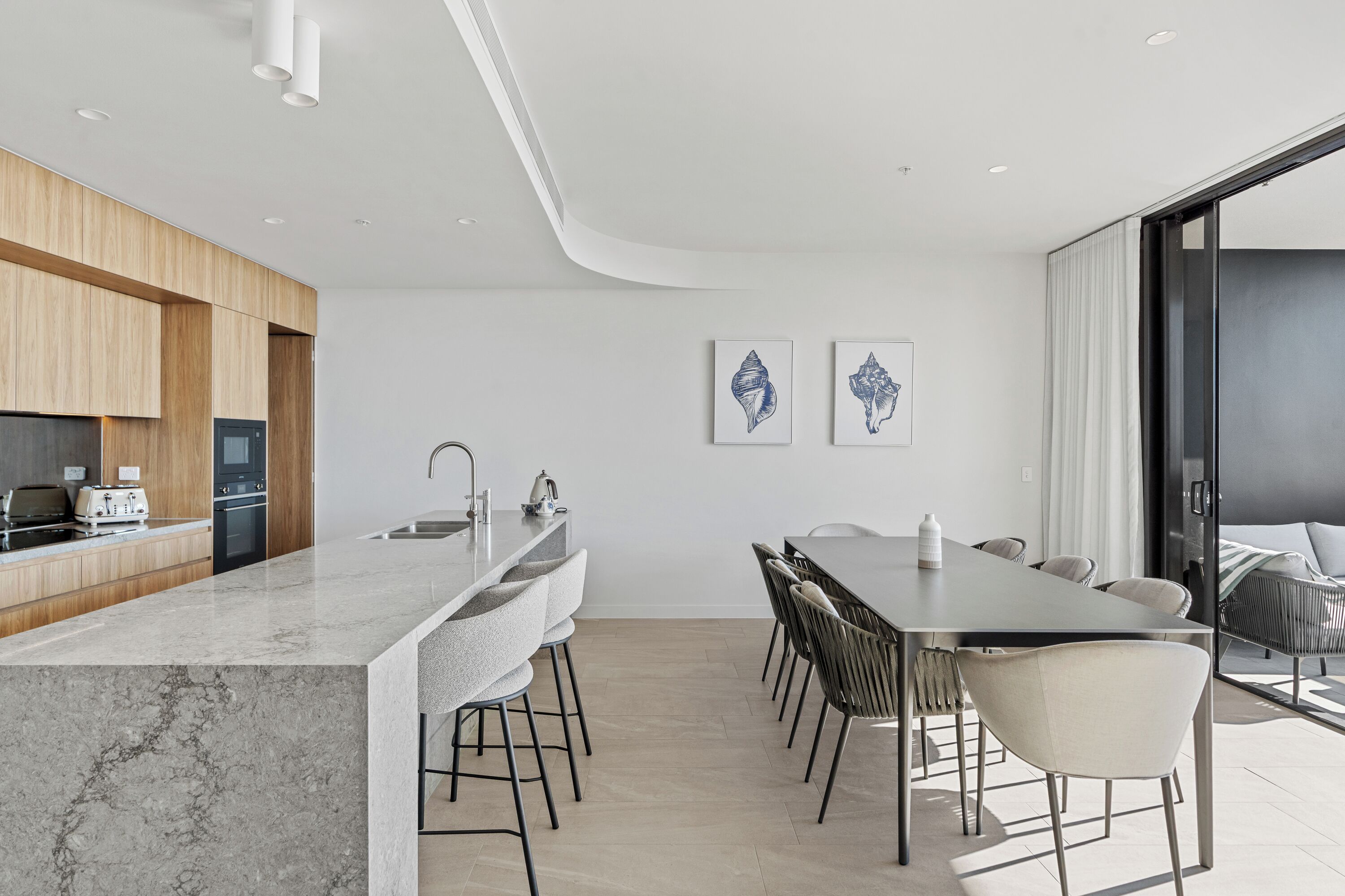 A modern kitchen with a marble countertop, wooden cabinets, and a dining area with a large table and chairs.