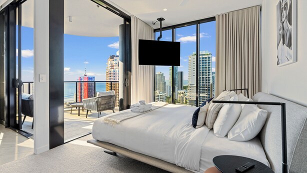 Ein modernes Hotelzimmer mit einem großen Bett, einem an der Wand montierten Fernseher und einem Balkon mit Blick auf die Stadt.