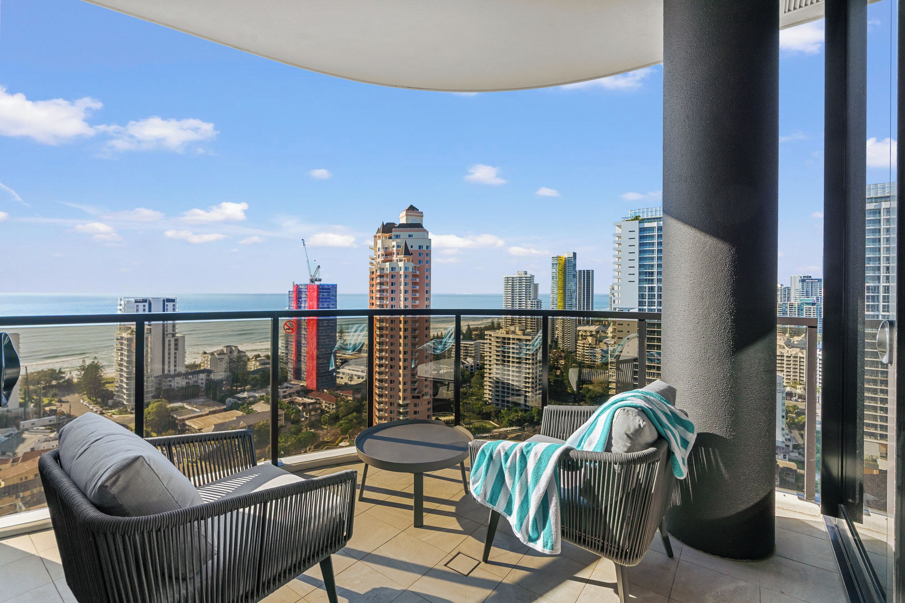 A balcony with wicker furniture, a round table, and a view of the city skyline and ocean.
