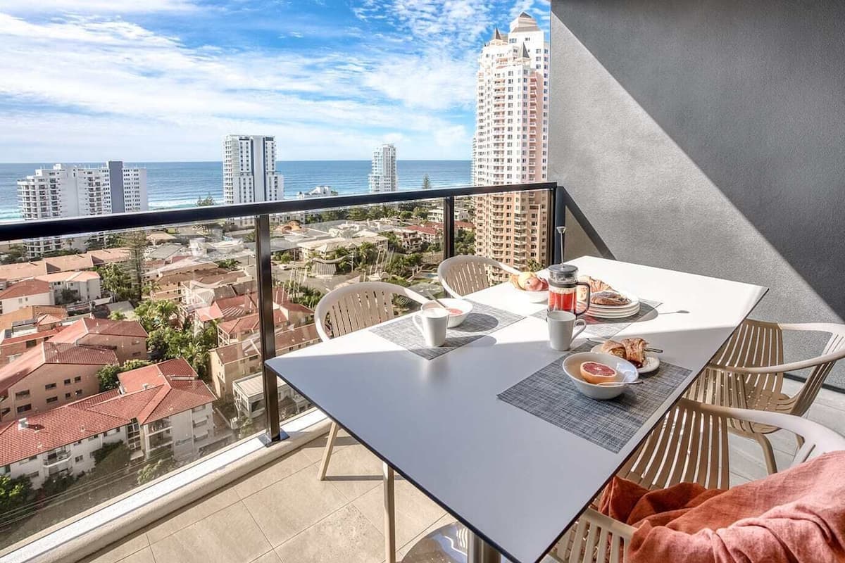 A balcony with a table set for breakfast, overlooking a coastal cityscape.