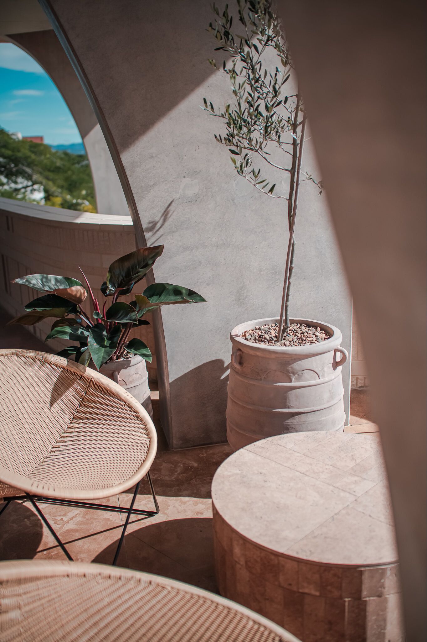 Varanda com planta em vaso, cadeiras de vime e mesa de pedra.