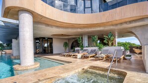 Ein moderner Poolbereich mit Liegestühlen, einem Whirlpool und einer überdachten Lounge.