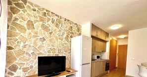 A modern kitchen with a stone wall, wooden cabinets, a built-in microwave, and a TV on a wooden stand.