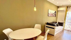 A modern living space with a round dining table, white chairs, a sofa, and a painting on the wall. - New international Loft, air-conditioned with pool and beach. (cambrils)