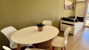 A modern living room with a round white table, white chairs, a potted plant, a sofa, and a painting on the wall. - New international Loft, air-conditioned with pool and beach. (cambrils)