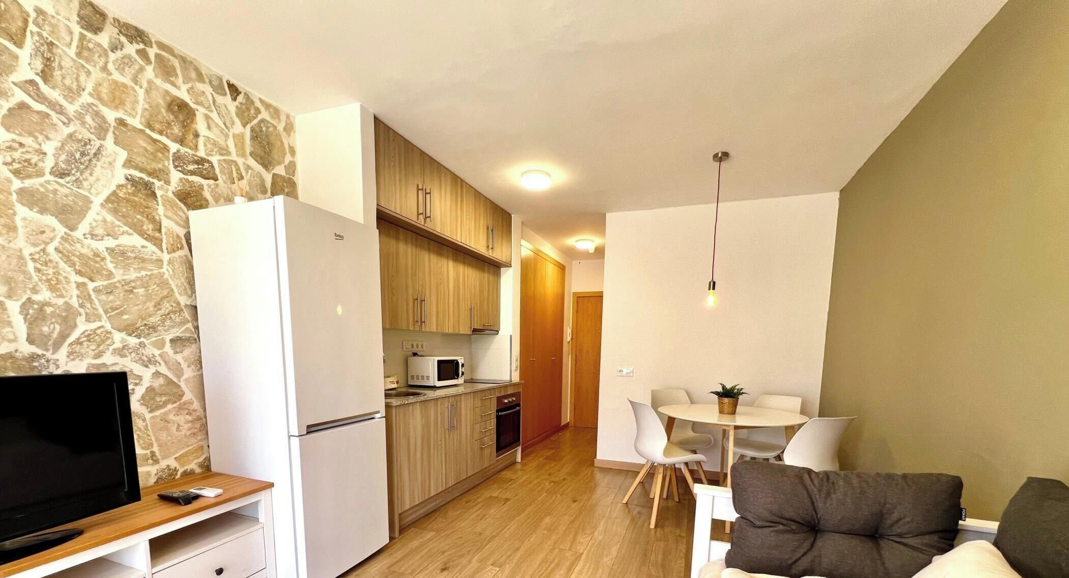Ein kompakter Wohnbereich mit Steinwand, einer Küchenzeile, einem Essbereich mit Tisch und Stühlen sowie einem Fernseher auf einem Holzboden.