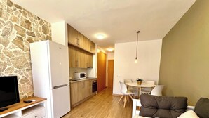 A compact living space with a stone wall, a kitchenette, a dining area with a table and chairs, and a TV on a wooden stand. - New international Loft, air-conditioned with pool and beach. (cambrils)
