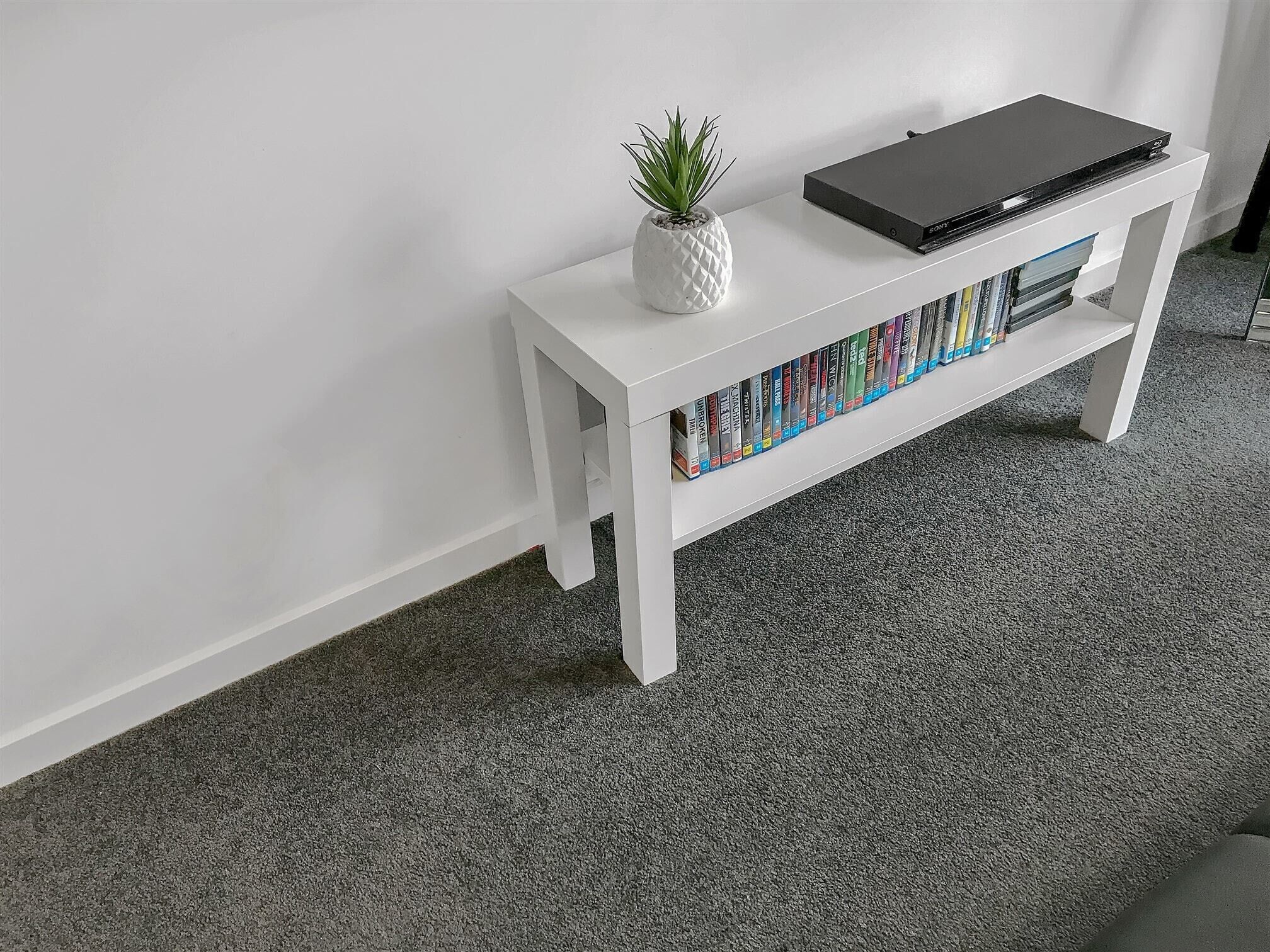 A white console table with a black laptop, a small potted plant, and a row of books.