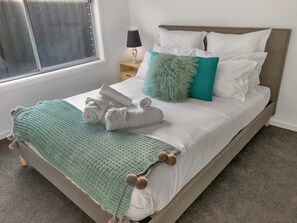A neatly made bed with white linens, a green knitted blanket, and decorative pillows. - Sleek Stylish Modern Close to Airport (Fraser Rise)