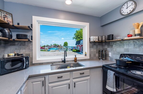 A modern kitchen with a large window, a microwave, a stove, and various kitchen utensils on the shelves.