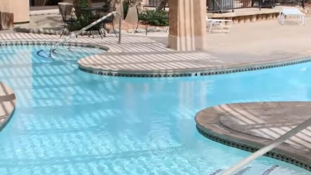Ein Schwimmbecken mit gefliestem Sonnendeck und einigen Liegestühlen im Hintergrund.