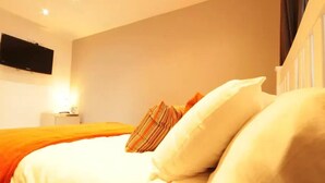 A hotel room with a bed, a flat-screen TV mounted on the wall, and a bedside table with a lamp. - Fantastic 2-Bed House in Hull. Garden, Sky tv. (Hull)