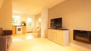 A spacious living area with a flat-screen TV on a wooden cabinet, a fireplace, and a kitchen in the background. - Fantastic 2-Bed House in Hull. Garden, Sky tv. (Hull)