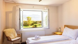Quarto de hotel com cama, uma cadeira, janela com vista e mesa de cabeceira.