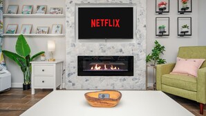 Ett vardagsrum med en öppen spis, en tv som hänger ovanför och en grön fåtölj.