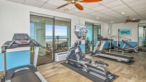 Ett gym med löpband, en crosstrainer och en motionscykel. Det har ett stort fönster med utsikt över havet.