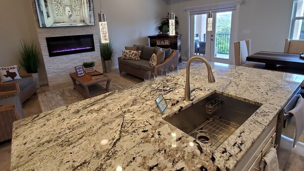 A spacious kitchen with a large island, a built-in oven, and a sink. There is a dining area with a table and chairs, and a living room with a sofa and a fireplace. - Hill Country Escape (Spring Branch)
