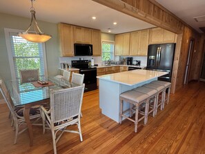 Una cocina moderna con armarios de madera, una isla central con taburetes de bar, una mesa de comedor con sillas y una lámpara colgante.