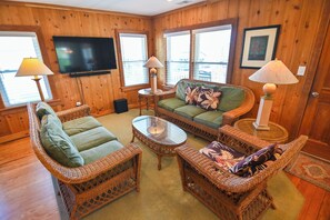 A cozy room with wicker furniture, a flat-screen TV, and large windows. - Top Floor Suite of classic 1940's Beach Cottage with porch & partial ocean view. (Wrightsville Beach)