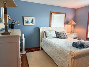 A bedroom with a bed, bedside table, lamp, and a picture on the wall.