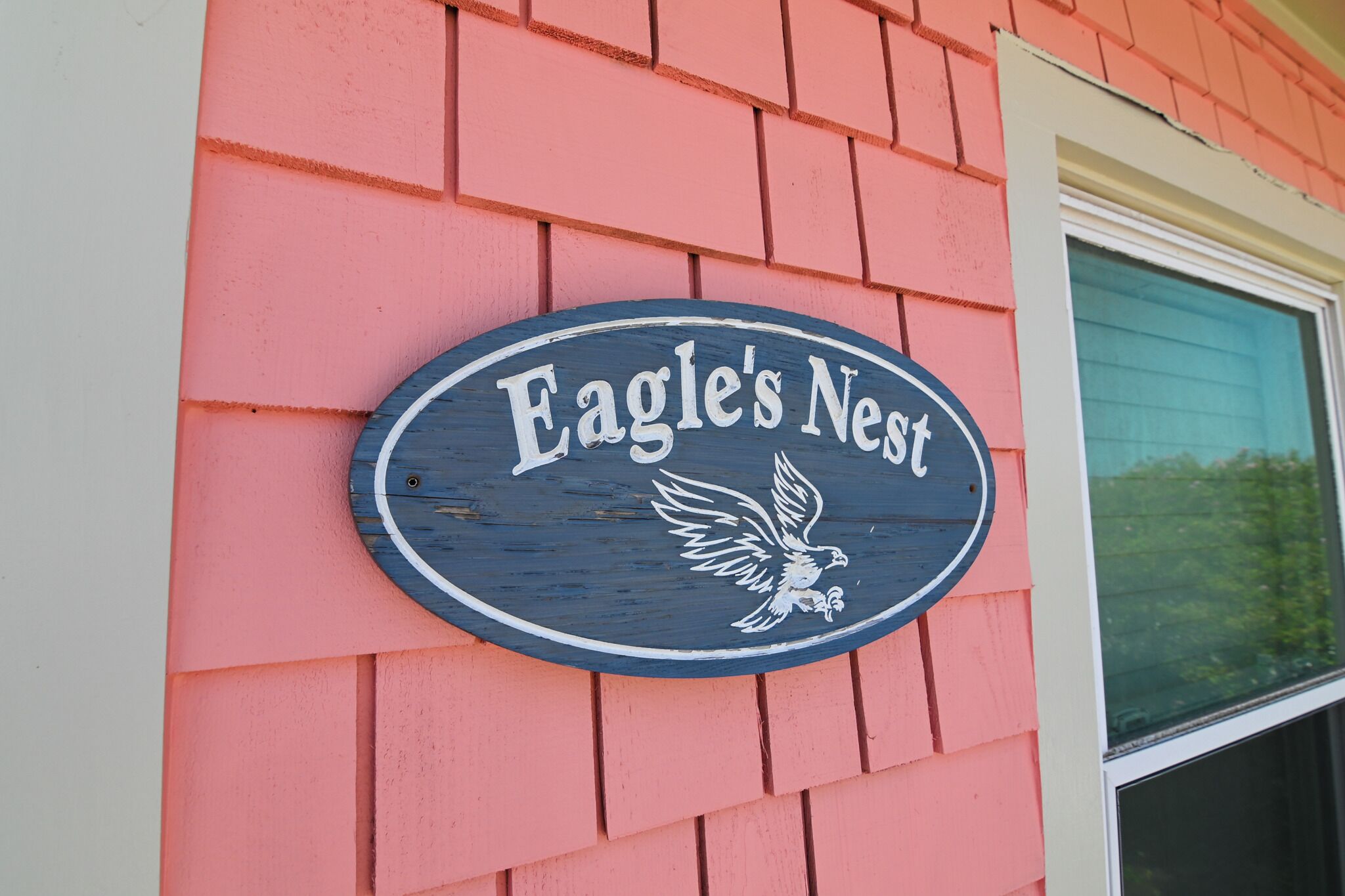 A sign with the text 'Eagle's Nest' and a bird illustration on a building with pink siding.