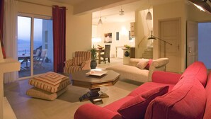 Un vaste espace de vie comprenant un canapé rouge, un fauteuil à rayures et une table basse. On aperçoit à l’arrière-plan un coin repas avec une table et des chaises.