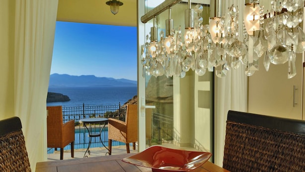 Un espace repas offrant une vue sur la mer et les montagnes, agrémenté d’un lustre et de meubles en osier.