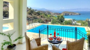 Un balcon avec une piscine, des meubles en osier et une vue sur la mer et les collines.
