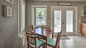 A dining area with a wooden table and chairs, a window with a view of greenery, and a sign above the door reading "THIS IS OUR HAPPY PLACE". - Trout Fishing Retreat on White River w/ Patio (Lakeview)