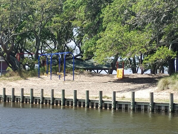 A park with a playground, a bench, and a sandy area near a body of water.
