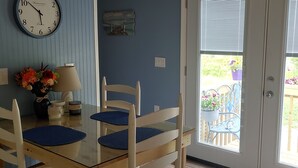 En matplats med ett träbord och stolar, en väggklocka, en vas med blommor och en utsikt genom en glasdörr till en uteplats.