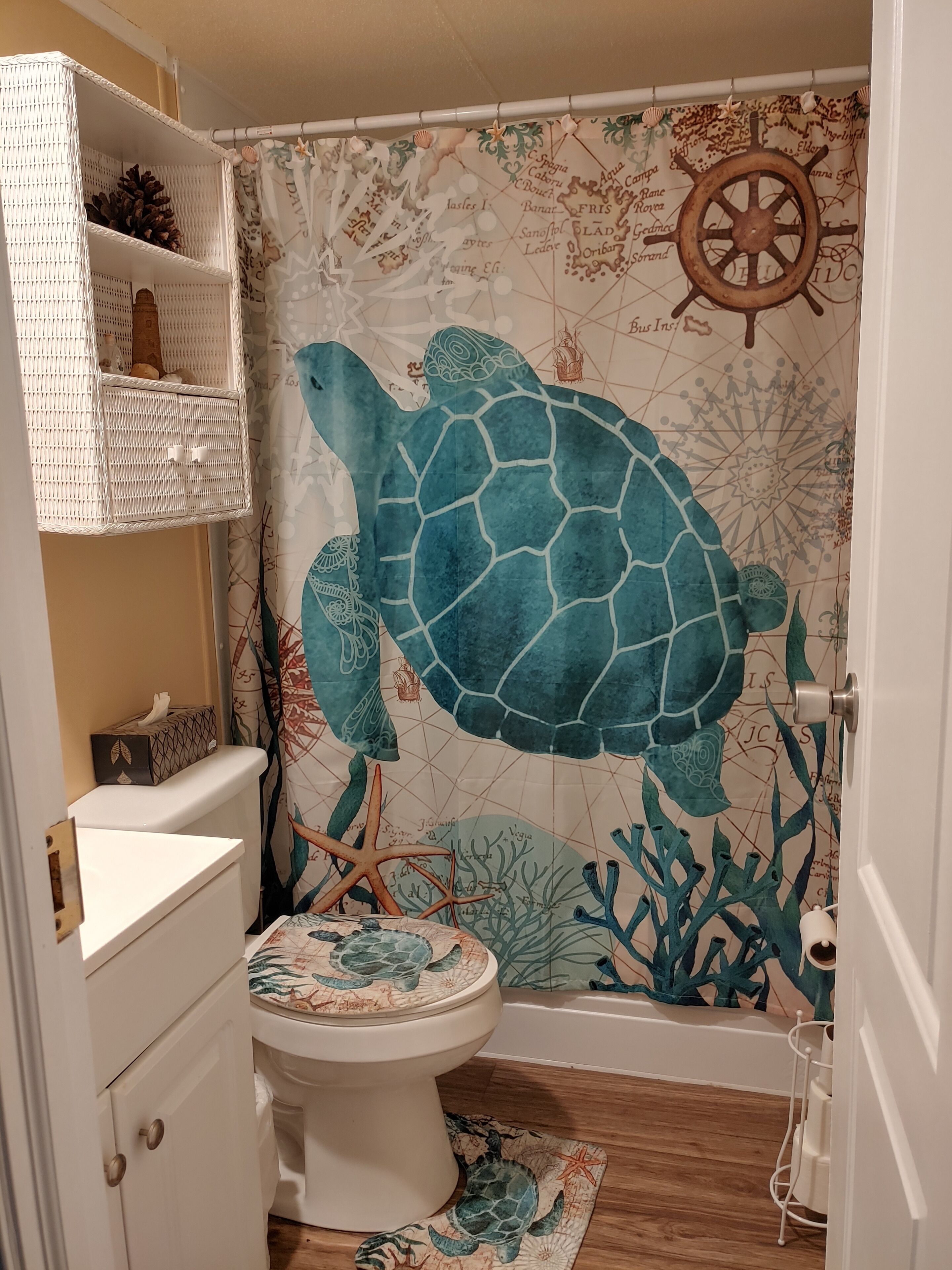 A bathroom with a nautical-themed shower curtain, a white toilet, and a wooden floor.