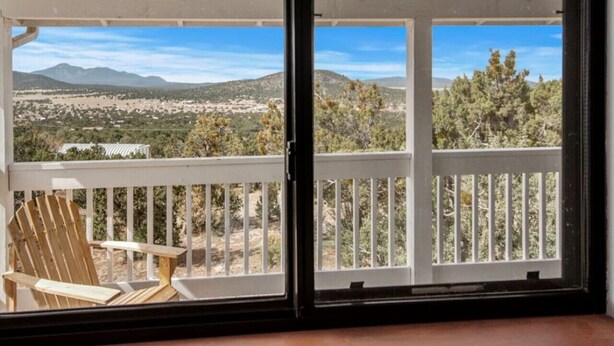 En balkon med en træstol, et hvidt gelænder og udsigt til et bjergrigt landskab.