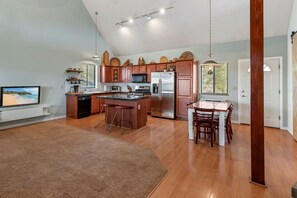 A spacious kitchen with wooden cabinets, a central island, and a dining area with a table and chairs. - Hillside Hideaway (Williams)