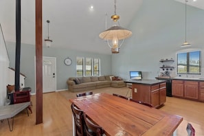 A spacious living area with a wooden dining table, a sofa, and a kitchen with a large window. - Hillside Hideaway (Williams)