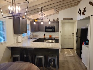 A modern kitchen with dark cabinets, a large island with bar stools, a microwave, and a refrigerator.