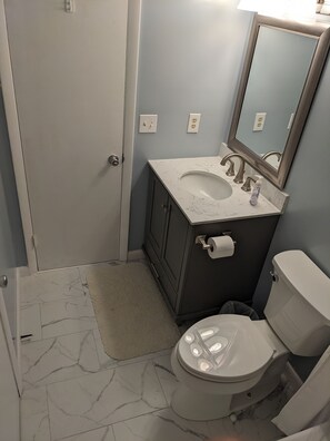 Une salle de bain équipée de toilettes, d’un lavabo, d’un miroir et d’un sol à motifs de marbre.