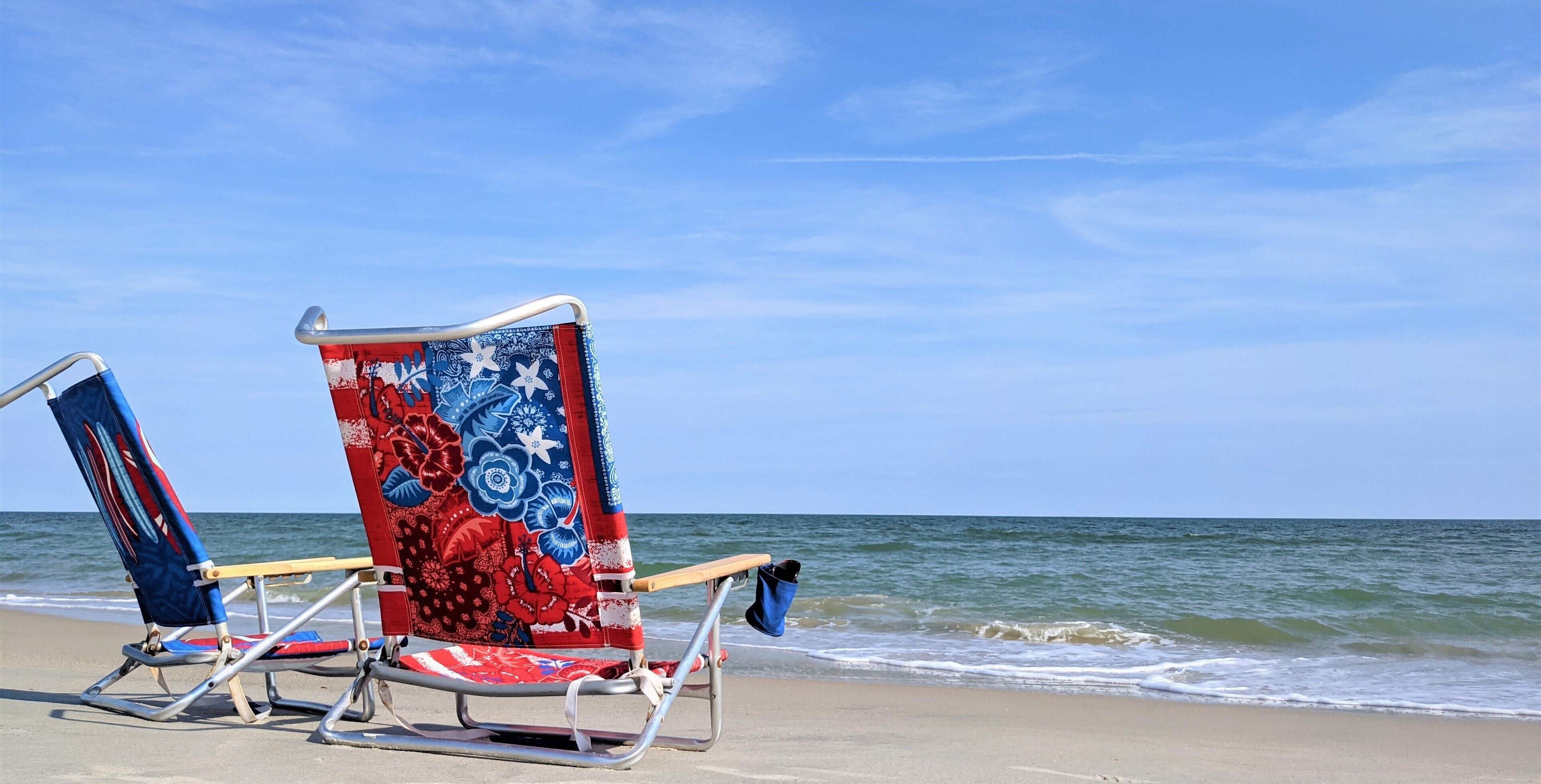 Two beach chairs with a floral pattern, positioned on a sandy beach with the ocean in the background.
